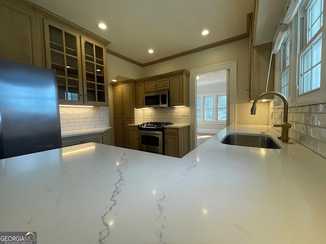 kitchen with light stone countertops, appliances with stainless steel finishes, sink, backsplash, and crown molding