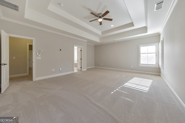 spare room with a tray ceiling, crown molding, and light colored carpet