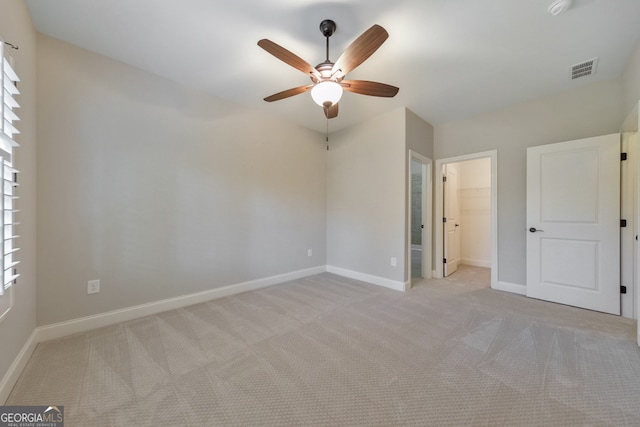 unfurnished bedroom featuring a closet, a walk in closet, light colored carpet, and ceiling fan