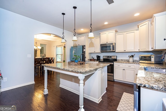 kitchen with hanging light fixtures, an island with sink, appliances with stainless steel finishes, and light stone counters