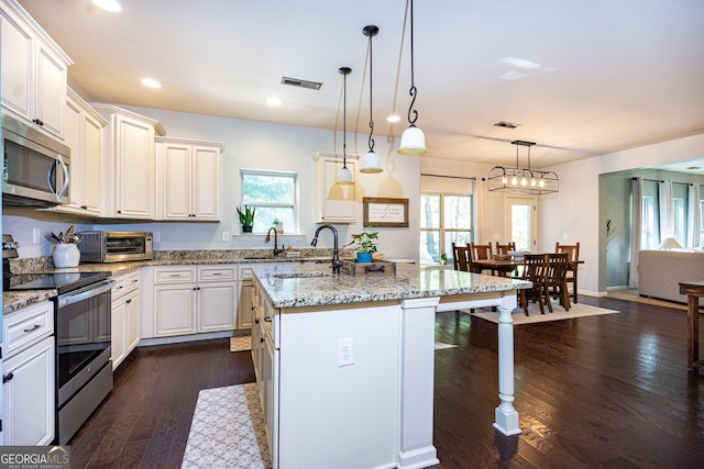 kitchen with dark wood-type flooring, sink, hanging light fixtures, appliances with stainless steel finishes, and a kitchen island with sink