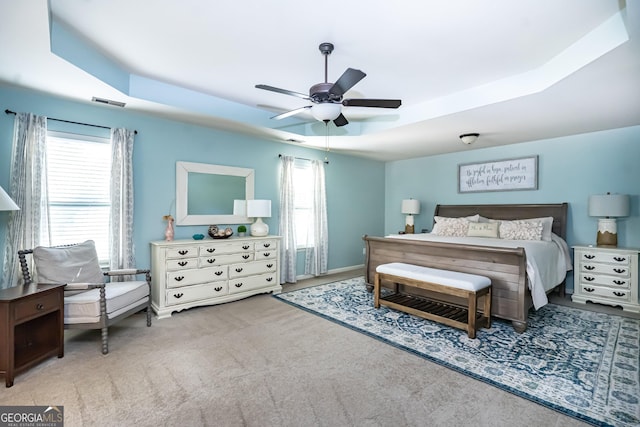 carpeted bedroom featuring ceiling fan, a raised ceiling, and multiple windows