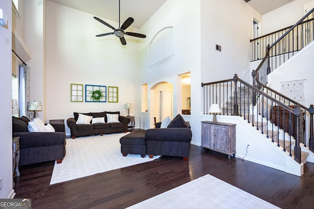 living room featuring dark wood-type flooring, a towering ceiling, and ceiling fan