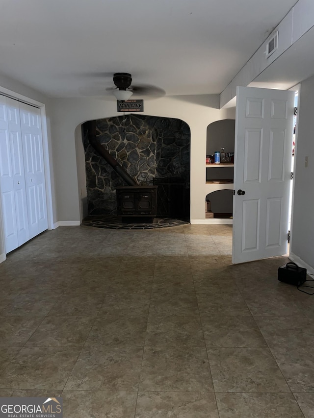 unfurnished living room with a wood stove and ceiling fan