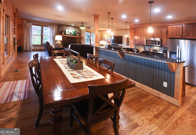 dining area with hardwood / wood-style floors, a large fireplace, and ceiling fan