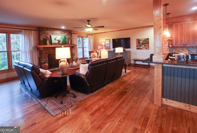 living room featuring crown molding, ceiling fan, wood-type flooring, and a stone fireplace