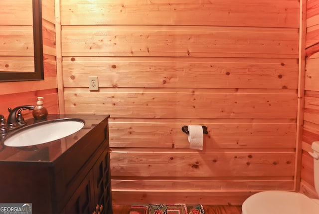 bathroom featuring vanity, toilet, and wooden walls