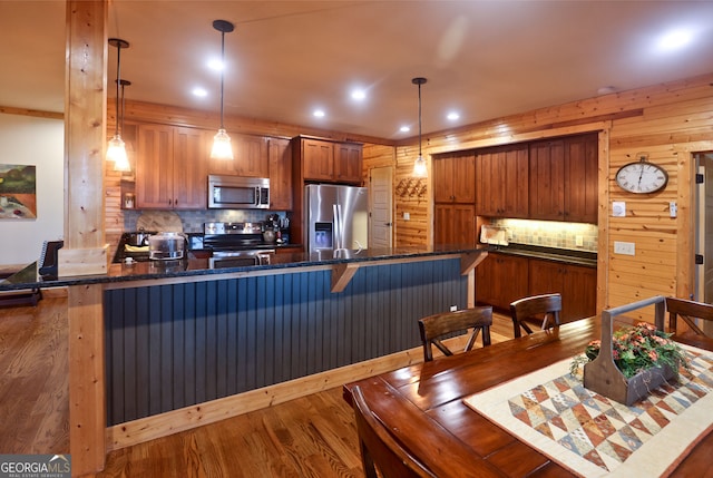 kitchen with a breakfast bar area, appliances with stainless steel finishes, hanging light fixtures, backsplash, and hardwood / wood-style floors