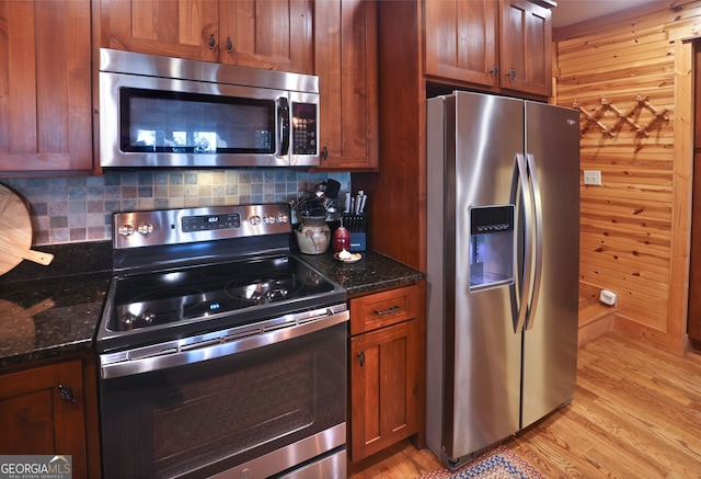 kitchen featuring tasteful backsplash, light hardwood / wood-style floors, stainless steel appliances, wooden walls, and dark stone countertops