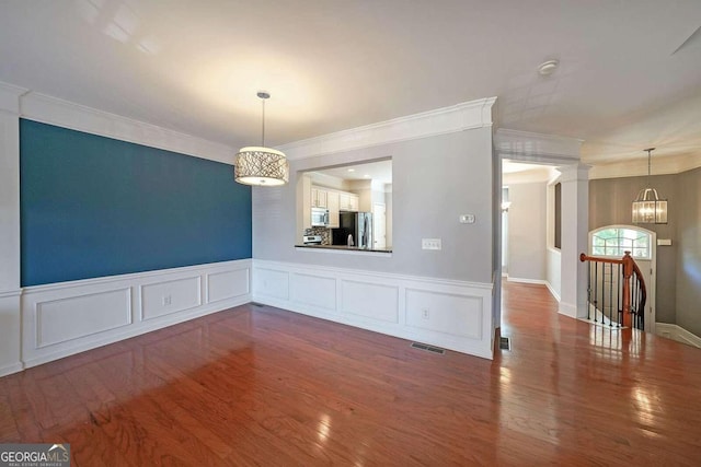 unfurnished dining area with hardwood / wood-style floors, a notable chandelier, crown molding, and decorative columns