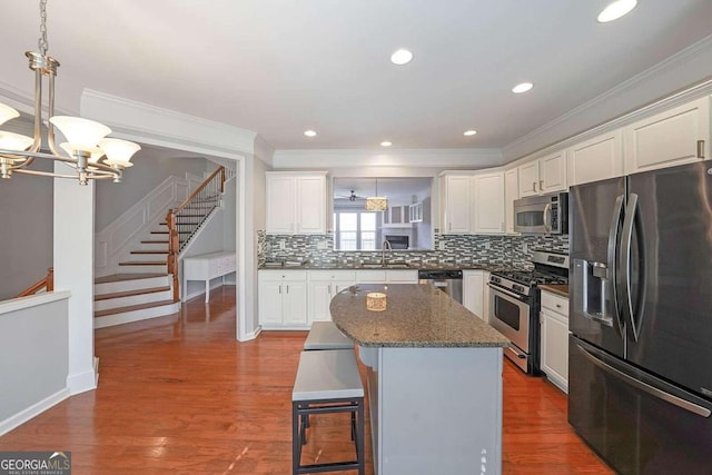 kitchen with appliances with stainless steel finishes, a center island, hardwood / wood-style floors, white cabinets, and ornamental molding