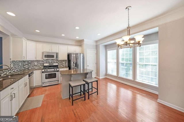 kitchen with a kitchen island, appliances with stainless steel finishes, white cabinetry, light hardwood / wood-style flooring, and sink