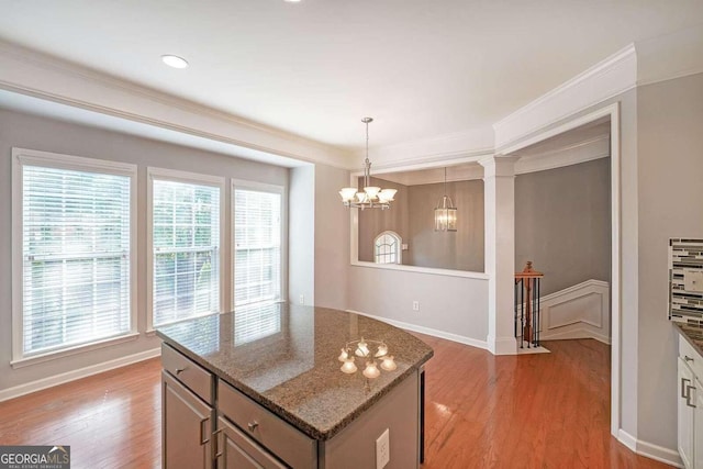 kitchen with ornate columns, light hardwood / wood-style flooring, dark stone countertops, ornamental molding, and pendant lighting