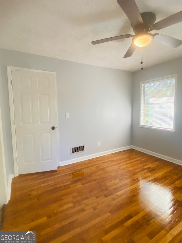 empty room with ceiling fan, a textured ceiling, and hardwood / wood-style floors