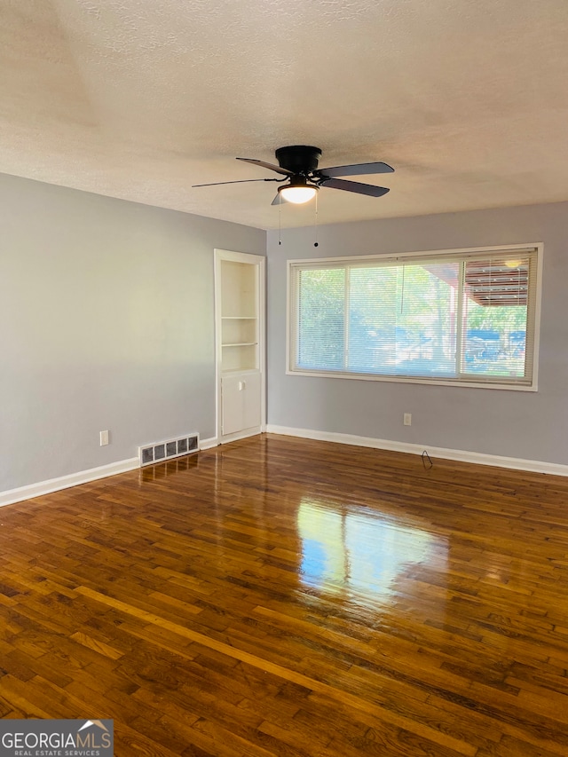 unfurnished room with built in shelves, ceiling fan, a textured ceiling, and dark hardwood / wood-style flooring