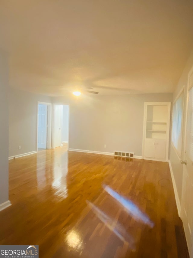 empty room featuring built in shelves and hardwood / wood-style floors