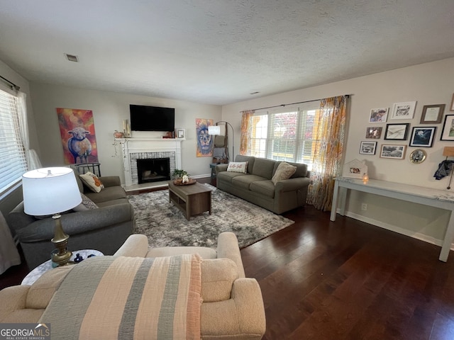 living room with dark wood-type flooring, a textured ceiling, and a brick fireplace