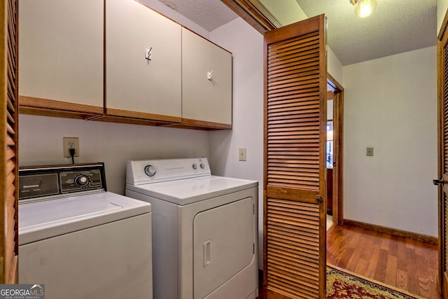 clothes washing area featuring hardwood / wood-style flooring, a textured ceiling, cabinets, and washing machine and clothes dryer