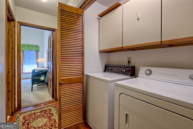 clothes washing area featuring a textured ceiling, cabinets, hardwood / wood-style floors, and washer and clothes dryer