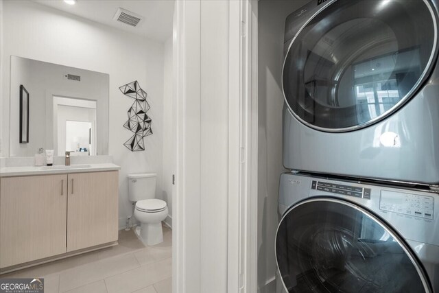 laundry room featuring light tile patterned floors, sink, and stacked washer and clothes dryer