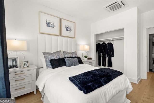 bedroom featuring light hardwood / wood-style flooring, a closet, and stacked washer / drying machine