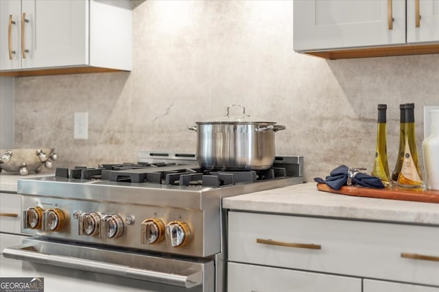 kitchen with decorative backsplash, white cabinets, and high end stainless steel range oven