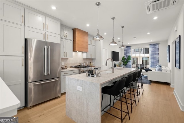 kitchen featuring white cabinets, hanging light fixtures, a center island with sink, light wood-type flooring, and premium appliances