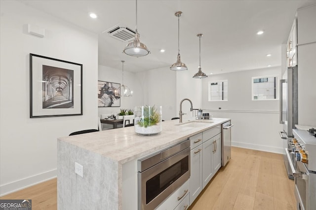 kitchen featuring appliances with stainless steel finishes, sink, light hardwood / wood-style floors, decorative light fixtures, and a kitchen island with sink