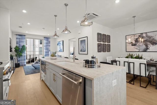 kitchen with appliances with stainless steel finishes, sink, hanging light fixtures, light hardwood / wood-style flooring, and a kitchen island with sink