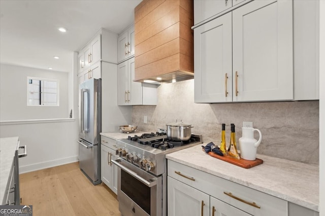 kitchen with custom range hood, light hardwood / wood-style floors, white cabinetry, and high end appliances