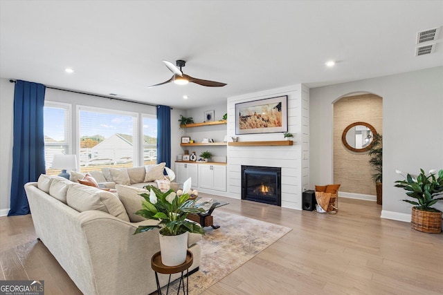 living room featuring light hardwood / wood-style floors, a large fireplace, and ceiling fan