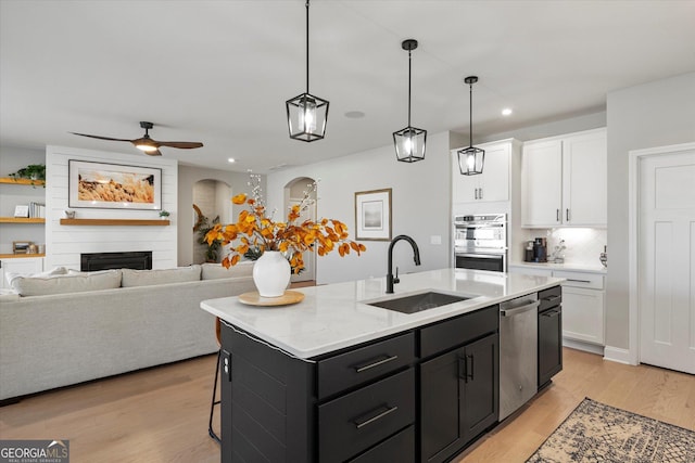 kitchen featuring a large fireplace, sink, a kitchen island with sink, stainless steel appliances, and white cabinets