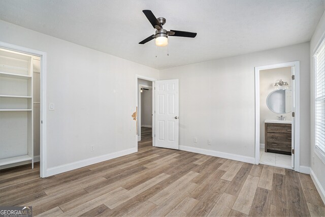 unfurnished bedroom with ceiling fan, a spacious closet, light hardwood / wood-style flooring, ensuite bathroom, and a closet