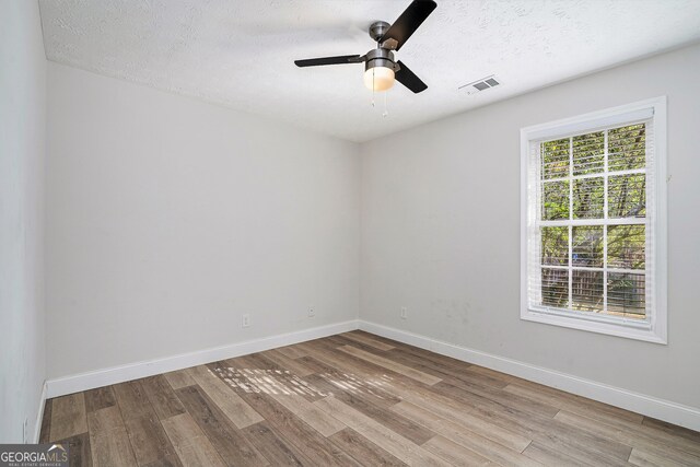 empty room featuring a textured ceiling, light wood-type flooring, and ceiling fan