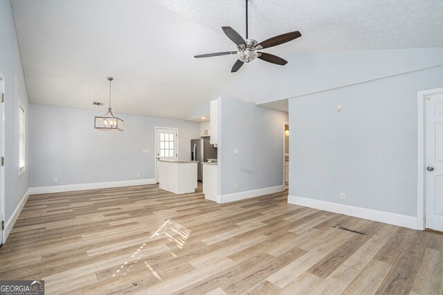 unfurnished living room featuring light hardwood / wood-style floors, a textured ceiling, lofted ceiling, and ceiling fan with notable chandelier