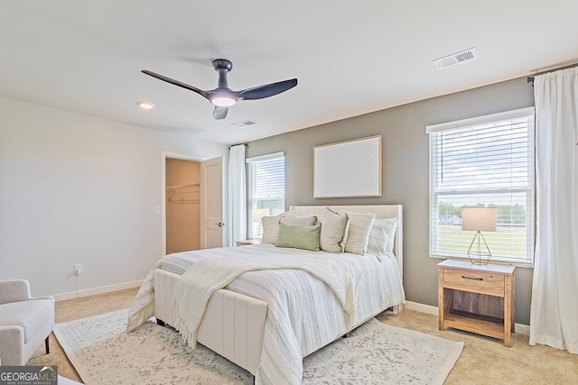 bedroom featuring light carpet, a walk in closet, a closet, and ceiling fan