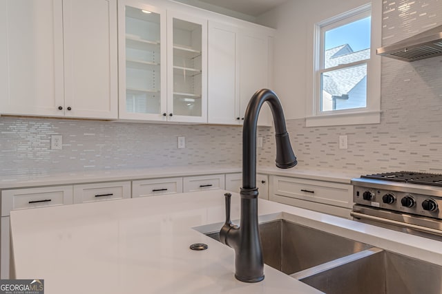 kitchen featuring wall chimney range hood, white cabinetry, sink, and backsplash