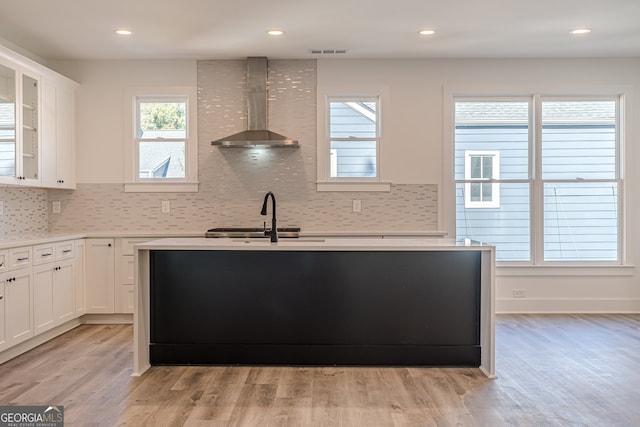 kitchen with sink, backsplash, white cabinetry, wall chimney exhaust hood, and light hardwood / wood-style flooring