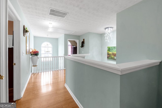 hall with a textured ceiling and light hardwood / wood-style flooring