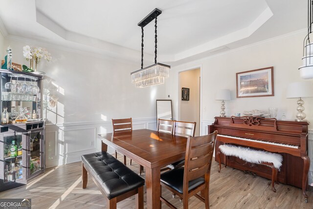 dining area with a raised ceiling, ornamental molding, and light hardwood / wood-style flooring