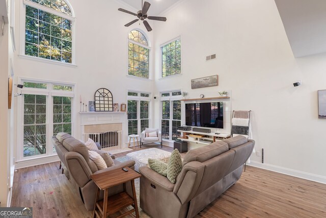 living room with a towering ceiling, light wood-type flooring, ceiling fan, and crown molding