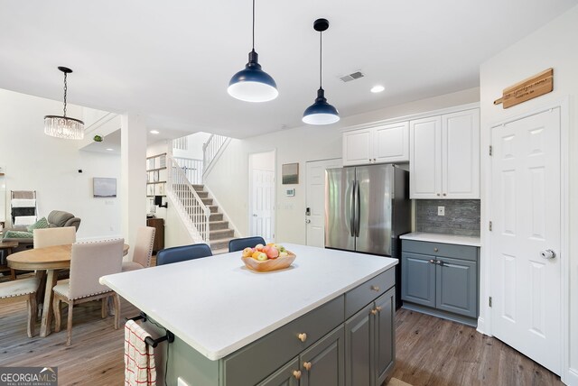 kitchen featuring stainless steel fridge, light wood-type flooring, decorative light fixtures, and white cabinetry