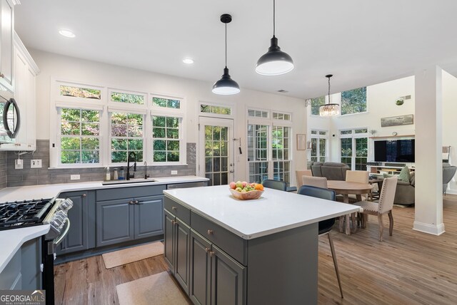 kitchen with light wood-type flooring, a healthy amount of sunlight, sink, stainless steel stove, and white cabinetry