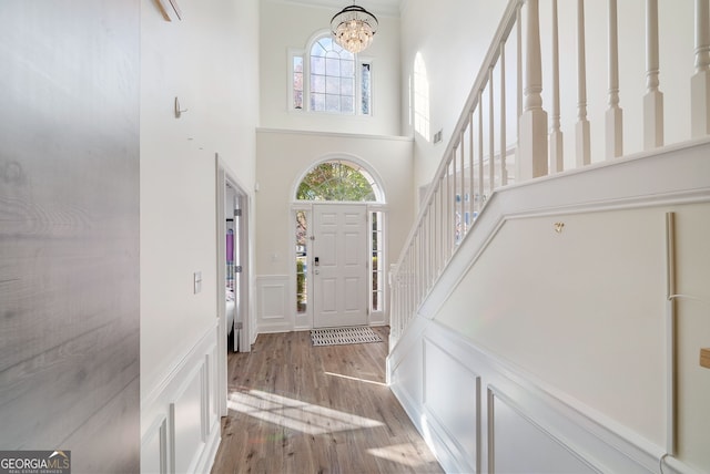 entrance foyer featuring wood-type flooring, a towering ceiling, and a notable chandelier