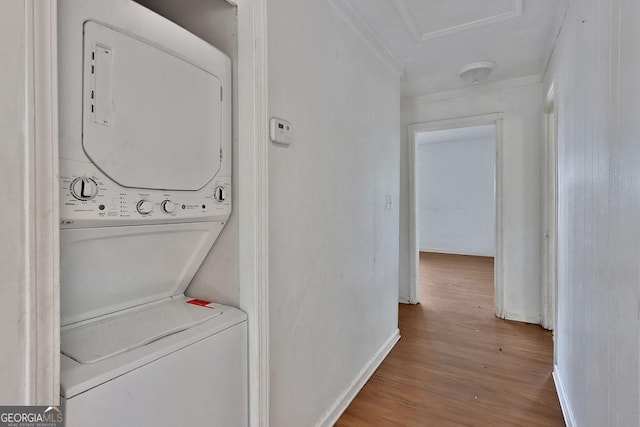 laundry room with stacked washer / dryer, crown molding, and hardwood / wood-style flooring