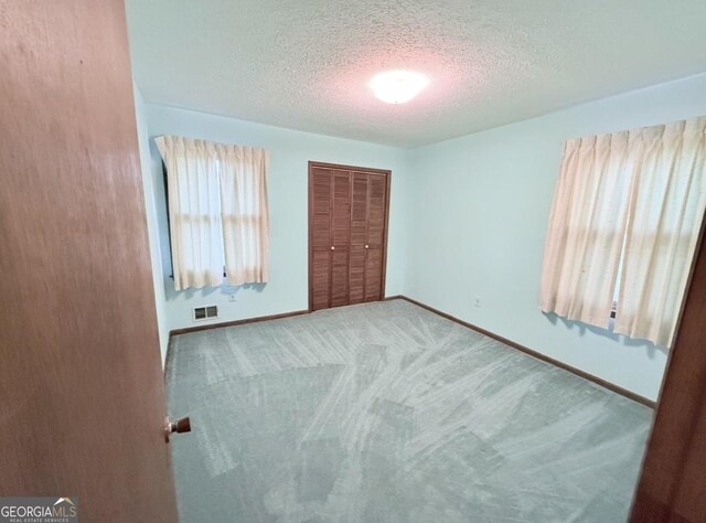 unfurnished bedroom with baseboards, visible vents, carpet floors, a closet, and a textured ceiling