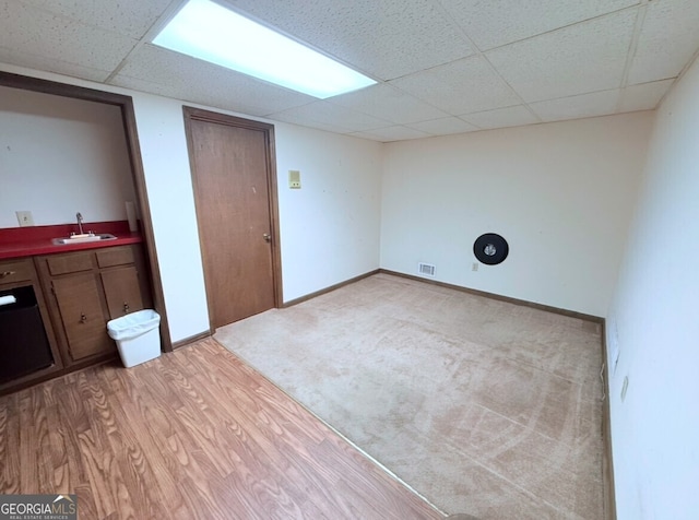 finished basement featuring visible vents, baseboards, a drop ceiling, light wood-type flooring, and a sink