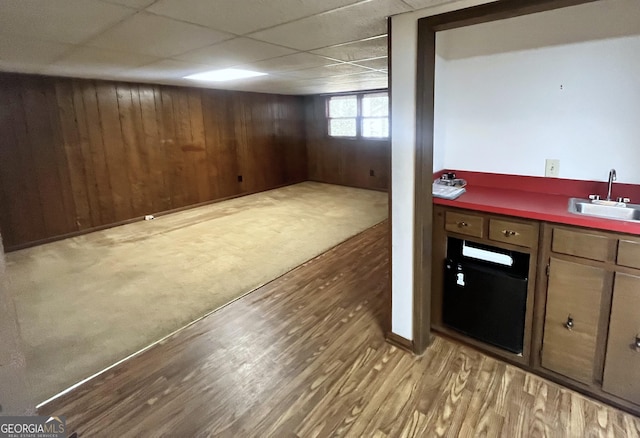 basement with a sink, a drop ceiling, wood finished floors, and wood walls