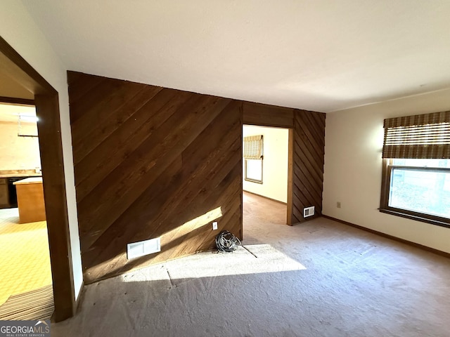 unfurnished living room with visible vents, carpet floors, wooden walls, and baseboards