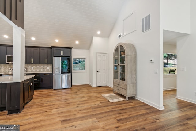 kitchen with high vaulted ceiling, dark brown cabinets, stainless steel fridge with ice dispenser, light wood-type flooring, and decorative backsplash